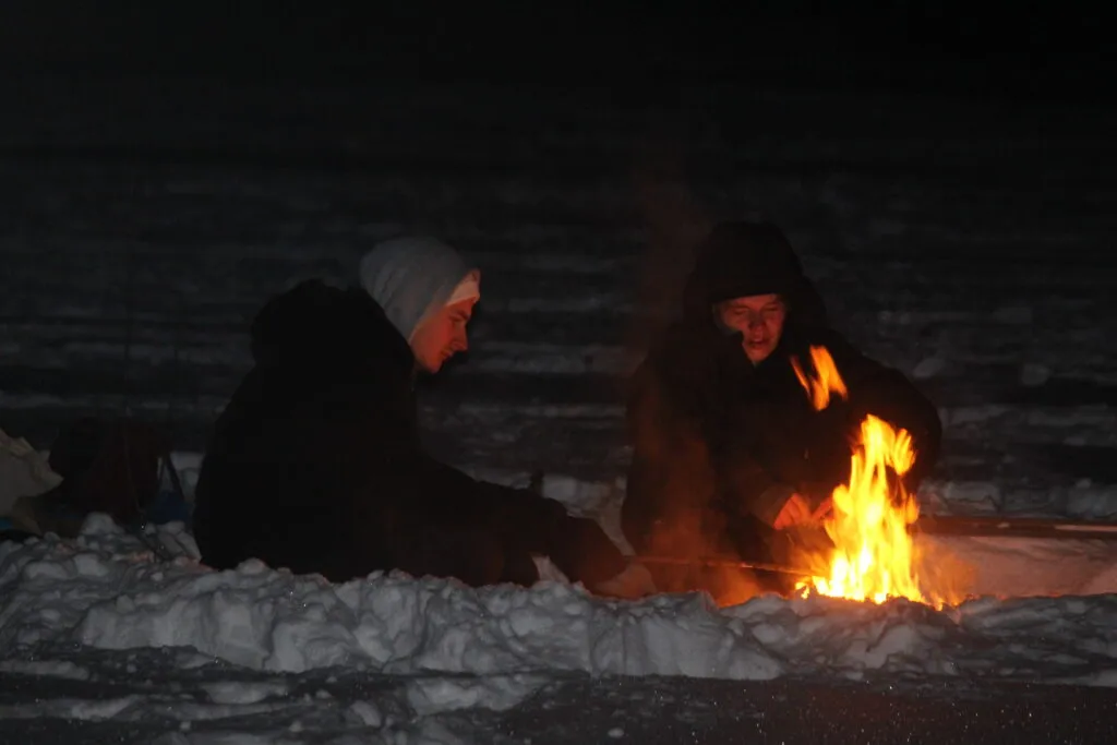 Two people sitting and warming themselves at a campfire
